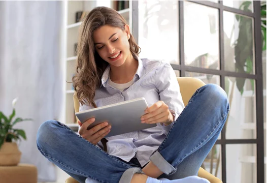 Una mujer joven sentada en su sala, revisando información en una tablet.