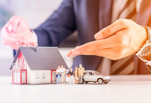 Manos de una persona mostrando piezas en miniatura sobre una familia en su hogar.