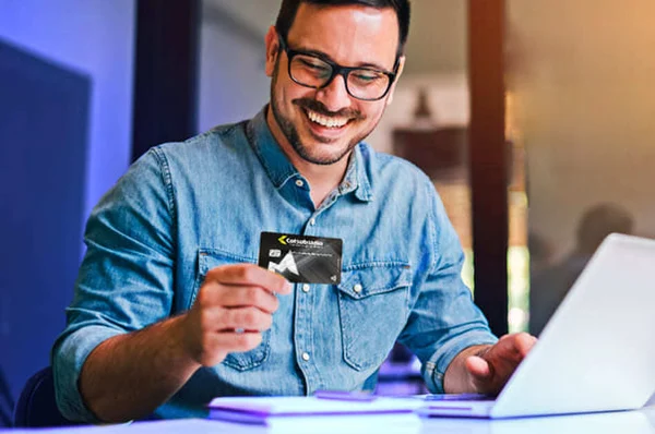 Hombre feliz realizando compras por internet con su  tarjeta multiservicios