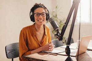 Una mujer locutora hablando frente a un computador portátil y un micrófono.
