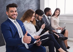 Hombre sonriente a lado de un grupo de personas, quienes buscan empleo.