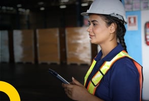 Una asesora en seguridad y salud en el trabajo sosteniendo una tablet mientras evalúa el entorno de su empresa.