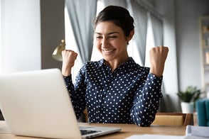Mujer feliz, sentada frente a su computador portátil.