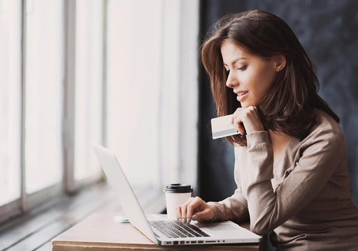 Una mujer con su tarjeta de crédito, pagando en línea en su computador portátil.