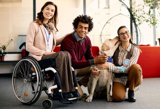 Una persona en silla de ruedas, acompañada de un perro y dos personas más.
