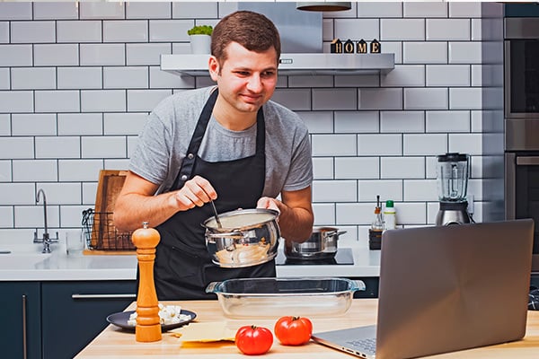 Hombre con una cuchara y una olla atiende exposición virtual desde su computador portátil.
