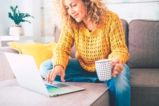 Mujer con una taza e café en su mano, revisando información en su computador portátil.