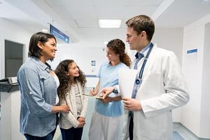 Madre e hija dialogando con un médico y enfermera en un hospital.