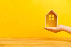 Una mano sosteniendo una casa pequeña de madera que representa los créditos de vivienda.