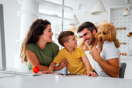 Una pareja, su hijo y su mascota jugando en la comodidad de su hogar gracias al seguro que le brinda Colsubsidio.