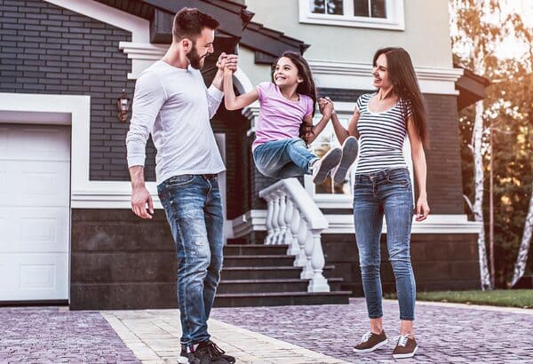 Un padre y una madre con su hija jugando fuera de su casa.