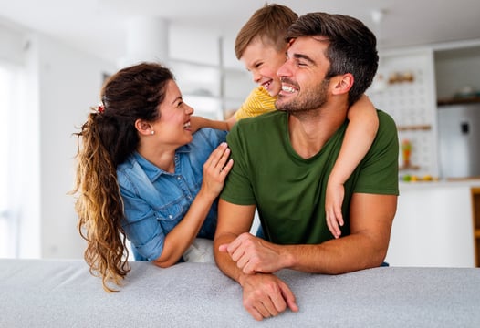 Una pareja y su hijo, disfrutando en la comodidad de su hogar gracias al seguro que le brinda Colsubsidio.