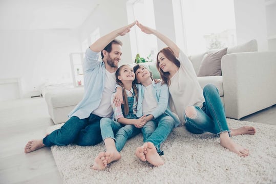 Dos padres y sus hijos formando un techo con sus manos, sentado en la sala de su casa.