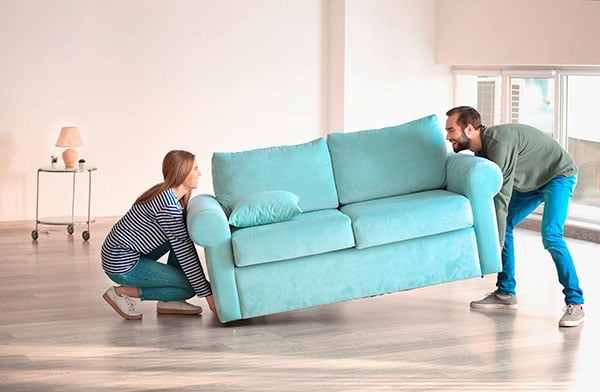 Pareja feliz cargando un sofá para instalarlo en su nuevo hogar.