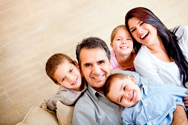 Familia feliz compuesta por madre y padre y sus tres hijos, sentados en la sala de su casa.