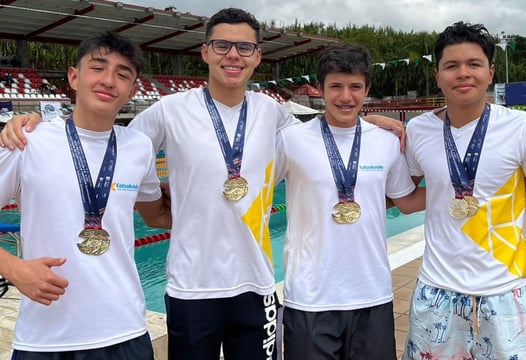 Cuatro jóvenes nadadores se abrazan y muestran sus medallas colgadas del pecho.