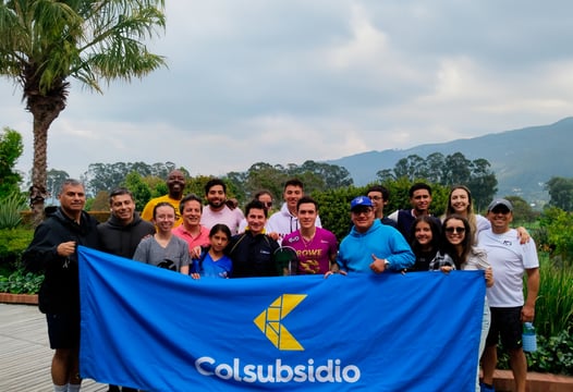 Grupo de hombres, mujeres y niños sonríen mostrando pancarta con logo de Colsubsidio.