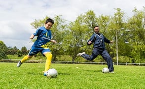 Un niño jugando fútbol con su entrenador deportivo.