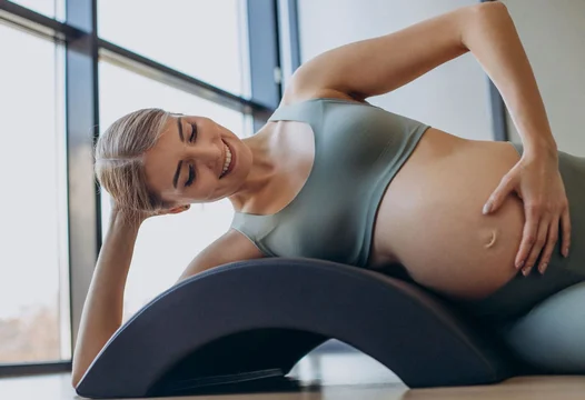 Una mujer embarazada realiza ejercicios de estiramiento sobre el suelo.
