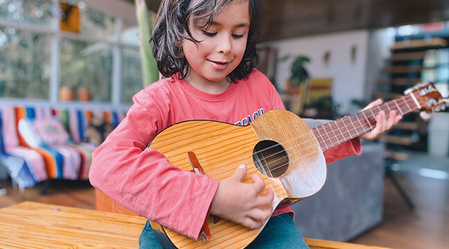 Niña sonriendo y tocando la guitarra en el programa de cuerdas