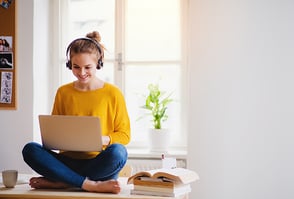 Una mujer sentada encima de un escritorio, trabajando en un computador portátil.
