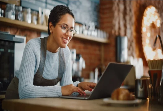 Una mujer sonriendo, trabajando frente a su computador portátil.