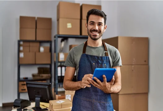 Un joven sonriendo en su sitio de trabajo, revisando información en una tablet.