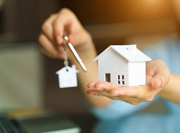 Una persona sosteniendo en una mano una casa de pequeña escala y en la otra mano sosteniendo unas llaves.