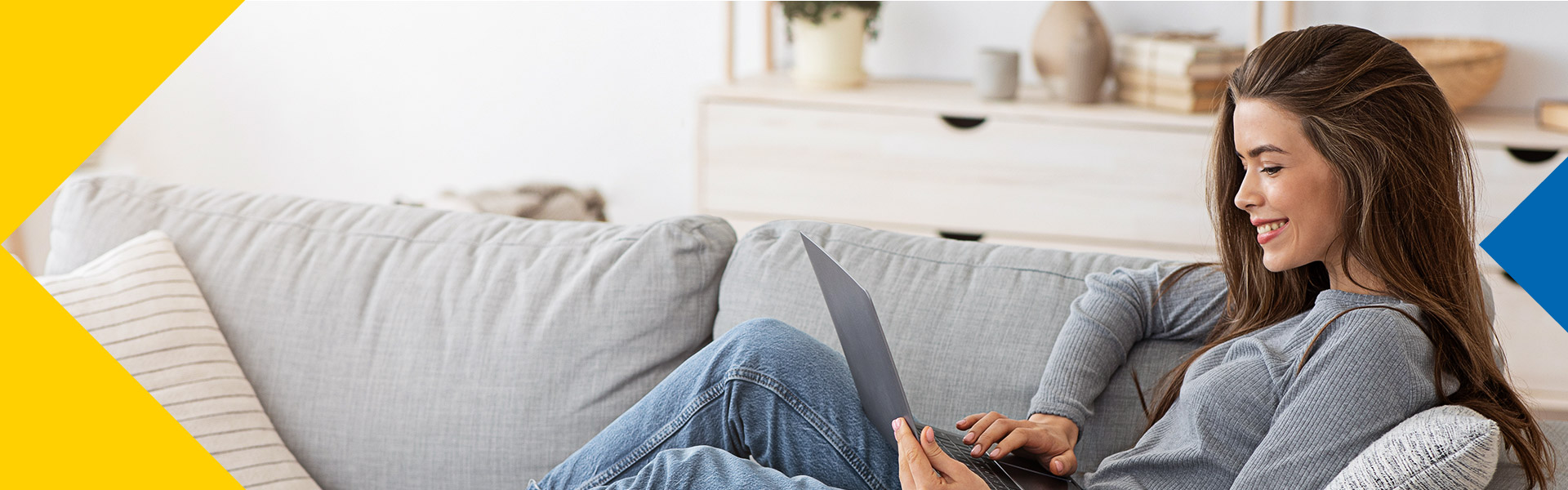 Una mujer sentada en el mueble de su casa, trabajando en su computador.