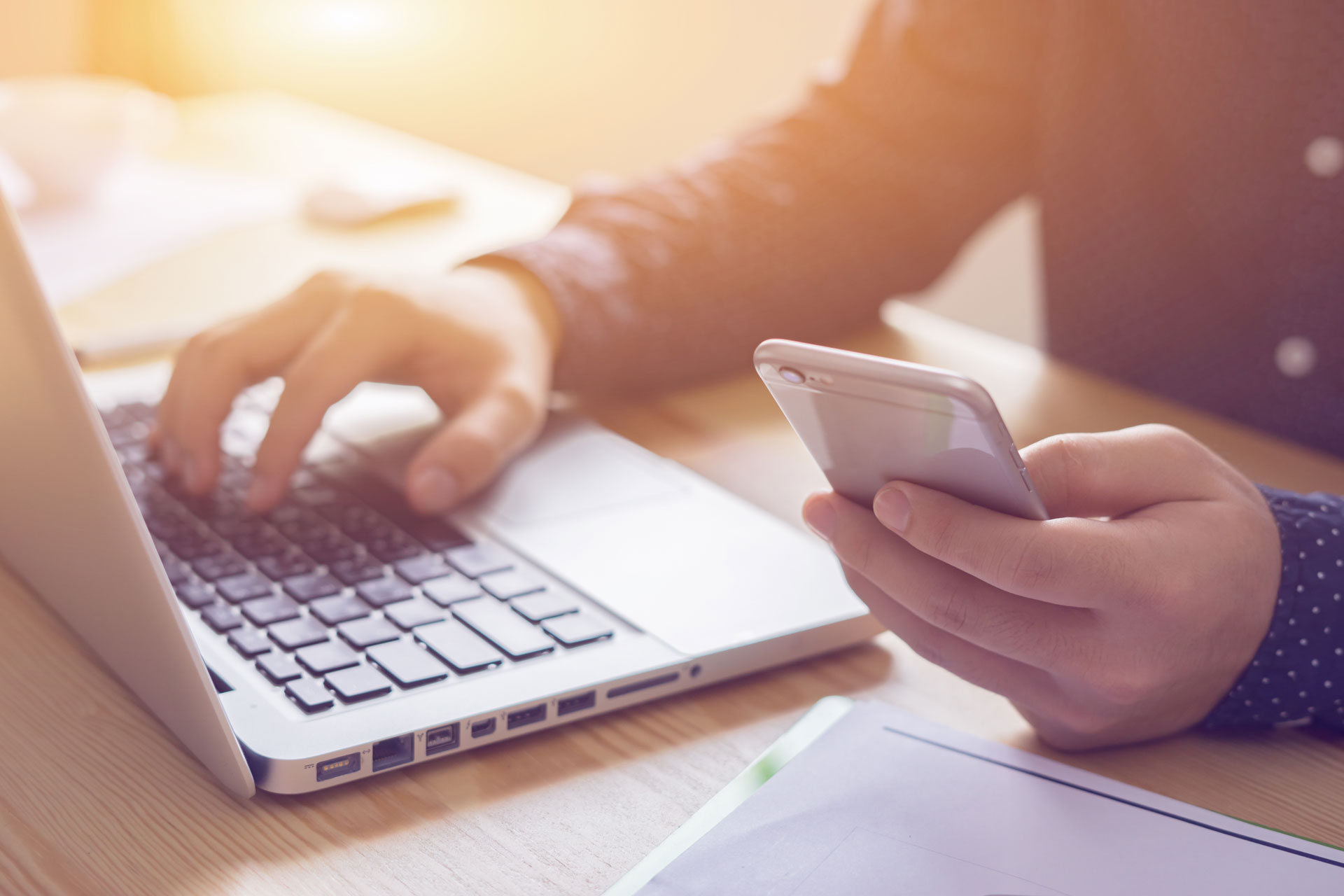 Una persona con un teléfono celular en la mano, ingresando datos en su computador portátil.