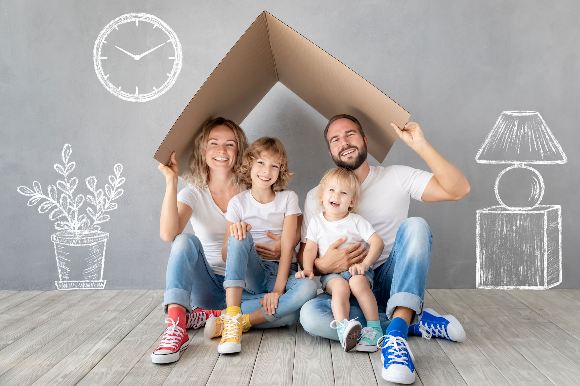 Familia feliz sosteniendo un techo de cartón, simulando su hogar.