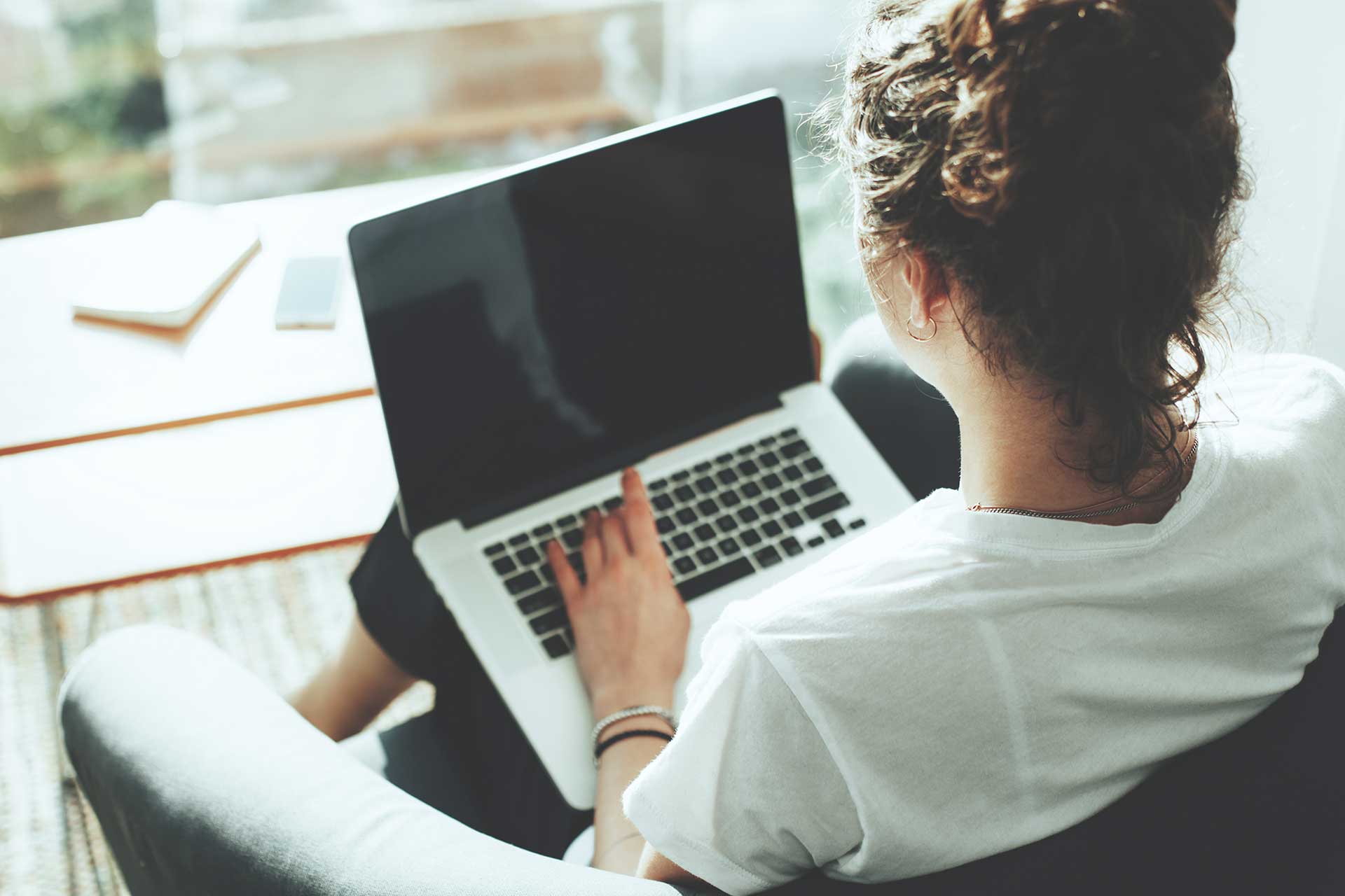 Una mujer sentada en su oficina, revisando información en un computador portátil.