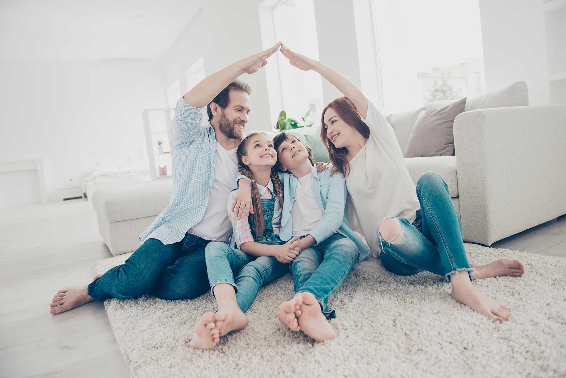 Dos padres y sus hijos formando un techo con sus manos, sentado en la sala de su casa.