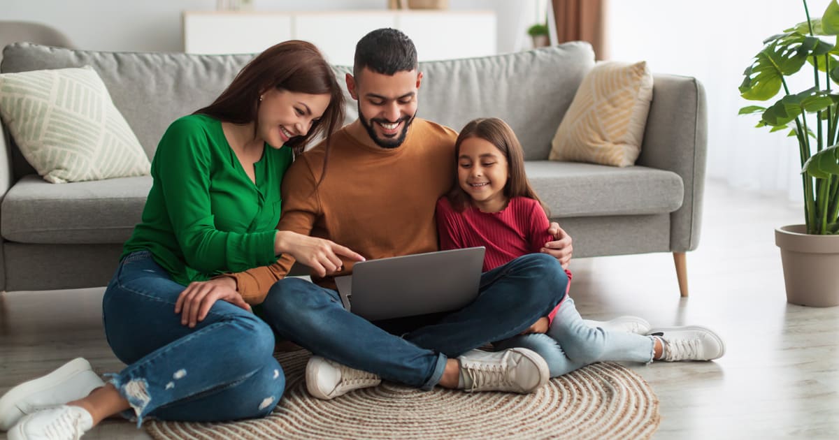 Pareja y su hija miran felices la pantalla de un computador portátil. 