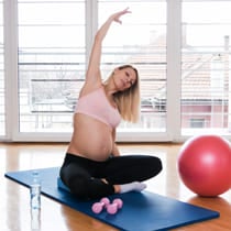 una mujer embarazada sentada en el suelo practica ejercicios de estiramiento para su espalda.