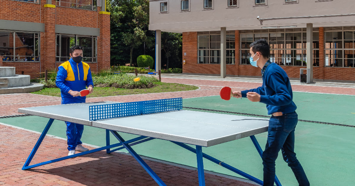 Dos estudiantes de los Colegios Colsubsidio jugando ping pong, al aire libre, en las instalaciones de Colegios Colsubsidio.