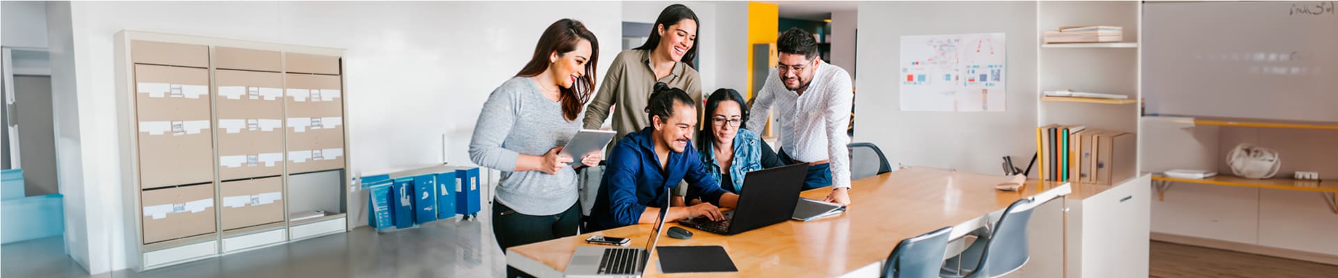 Cinco personas trabajando en sus dispositivos electrónicos en una sala de juntas.