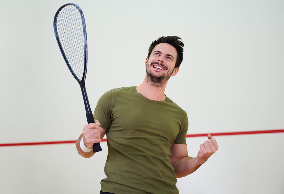 Un hombre feliz sosteniendo su raqueta y entrenando squash en Colsubsidio.