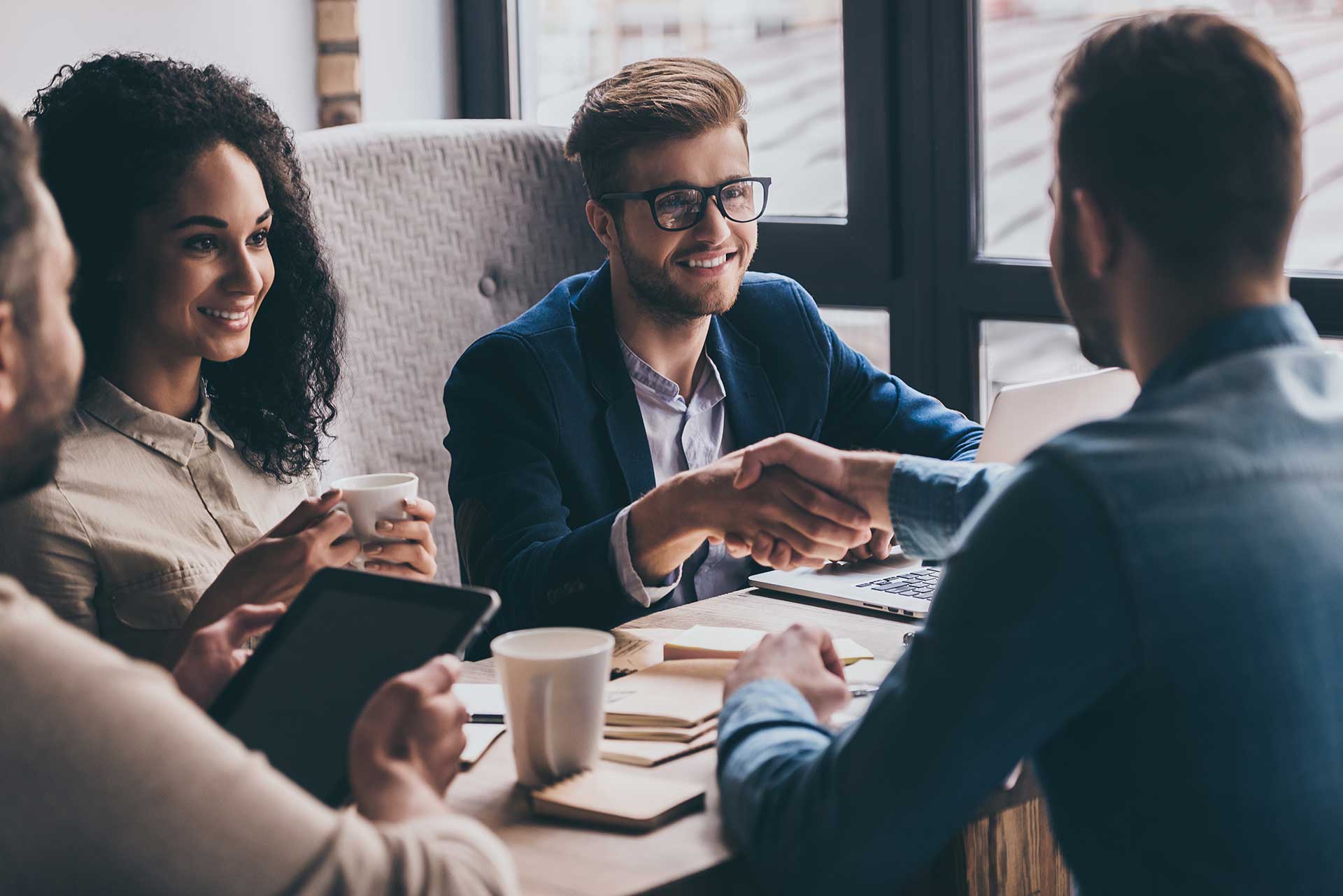 Dos personas estrechando sus manos, junto a su equipo de trabajo.